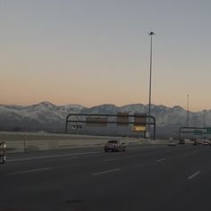 cars are driving down the highway in front of snow - capped mountain range at dusk