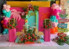 a table topped with lots of colorful balloons and flowers in front of a pink wall