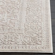 a white rug with an intricate design on the top and bottom corner, sitting on a wooden floor