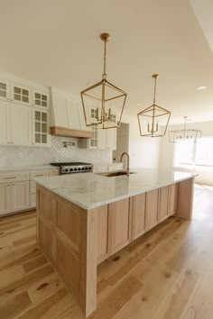 a large kitchen with an island in the middle and two hanging lights on the ceiling