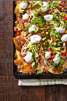 a tray filled with nachos and toppings on top of a wooden table