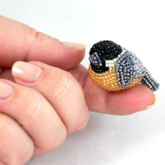 a tiny beaded bird sitting on top of someone's finger in front of a white background