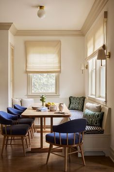 a dining room table with blue chairs and a bench in front of the window,