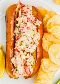 a hot dog with cole slaw and chips on a plate next to lemon wedges