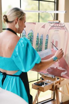 a woman in a blue dress painting on an easel