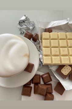 a cup of coffee and some chocolates on a white plate next to silver foil