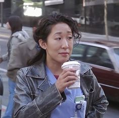 a woman is walking down the street with a cup in her hand and looking at something