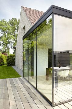 a glass walled patio with table and chairs on the decking next to an outdoor dining area