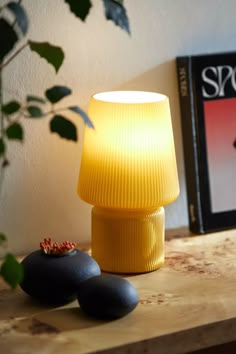 a yellow lamp sitting on top of a wooden table next to two black rocks and a plant