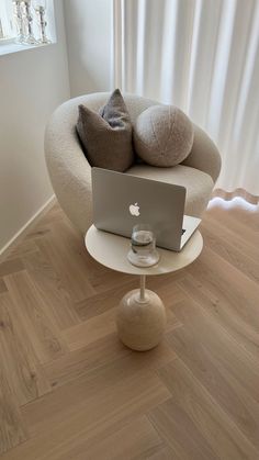 an apple laptop sitting on top of a white table in front of a chair with pillows