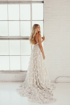 a woman standing in front of a window wearing a wedding dress with flowers on it