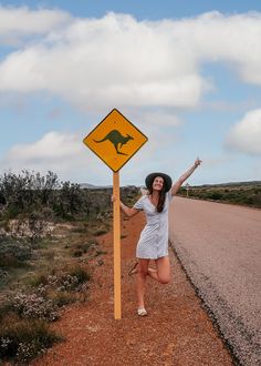 a woman standing next to a yellow kangaroo crossing sign on the side of a road