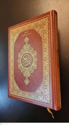 an old book with arabic writing on the cover and gold trimmings, sitting against a black wall