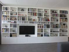 a living room filled with lots of white bookshelves and a flat screen tv