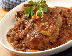 a white bowl filled with meat covered in sauce and garnishes on top of a wooden table