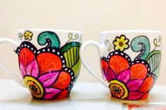 two coffee mugs decorated with colorful flowers are sitting side by side on a table