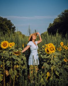 a woman standing in a field of sunflowers with her arms behind her head