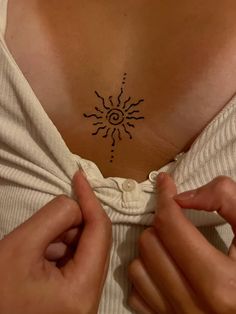 a woman's chest with a sun tattoo on her left side, and two hands holding