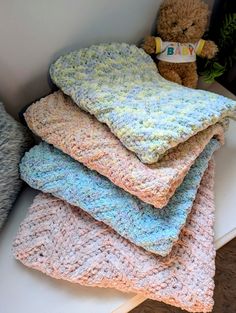 a pile of crocheted blankets sitting on top of a white table next to a teddy bear