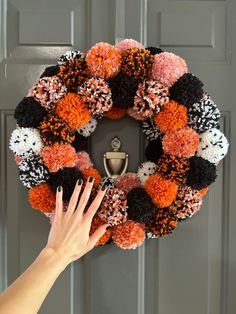 a woman's hand on the front door holding up a wreath with pom - poms