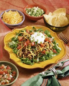 a yellow plate filled with taco salad next to bowls of salsa and tortilla chips