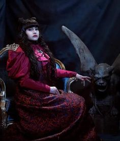 a woman sitting in a chair with horns on her head and wearing a red dress