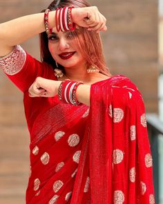 a woman in a red sari is holding her hands up to her head and looking at the camera