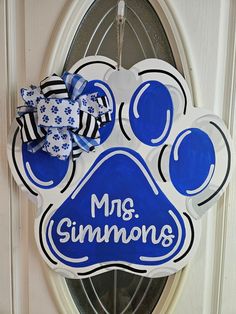 a blue and white dog paw shaped door hanger with the words mr simmons on it