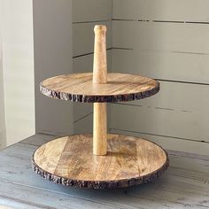 two tiered wooden cake stand on top of a white wood floor next to a wall