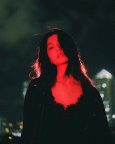 a woman with long hair standing in front of a cityscape at night time