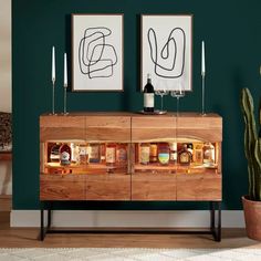 a wooden cabinet sitting next to a cactus in front of two pictures on the wall