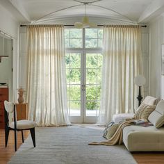 a living room filled with furniture and a large window covered in white curtained drapes