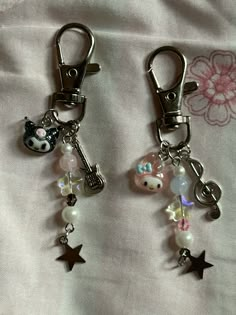 two keychains with charms attached to them sitting on a bed covered in white sheets