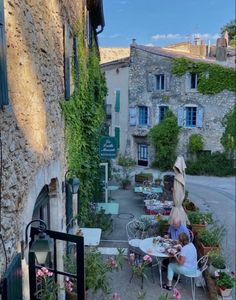 two people sitting at an outdoor table in front of a stone building with ivy growing on it