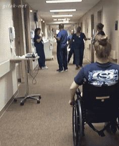 a man in a wheel chair walking down a hospital hallway with other people nearby on either side of the corridor