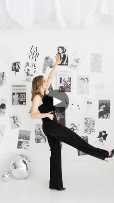 a woman standing in front of a wall with pictures on it and holding her leg up