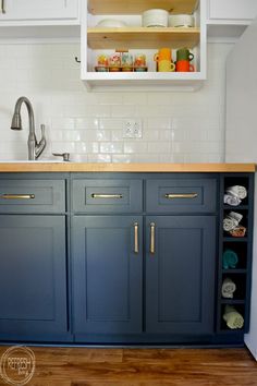 a kitchen with blue cabinets and white cupboards on the counter top, next to a wooden floor