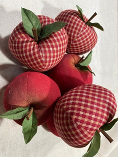 four red apples with green leaves sitting on a white cloth covered tablecloth, next to each other