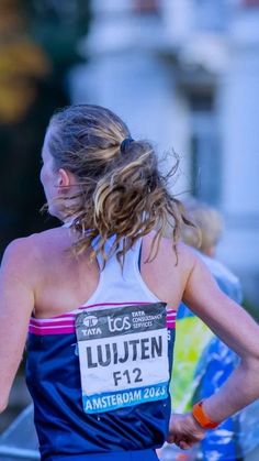 a woman with her back to the camera, running in a marathon wearing a blue and white tank top