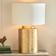 a gold lamp sitting on top of a table next to two books and a cat figurine