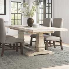 a dining room table with chairs and a vase on it's centerpiece in front of windows