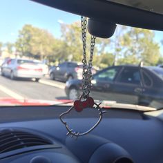 a hello kitty keychain hanging from the dashboard of a car with cars in the background