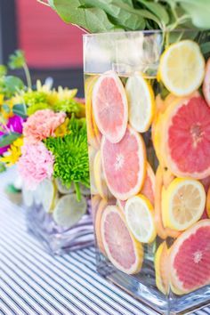 a glass vase filled with lemons on top of a table next to flowers and greenery