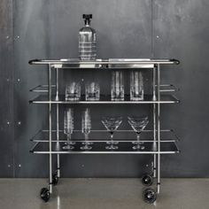 a bar cart with glasses and bottles on the top shelf in front of a gray wall