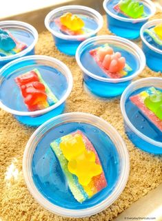 there are many small plastic plates with food in them on the sand and some water