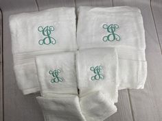 four white towels with green monogrammed letters on them sitting on a wooden floor