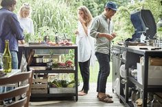 a group of people standing in a kitchen next to an outdoor table with food on it