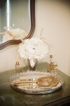 there is a silver tray with flowers in it and a mirror on the wall behind it