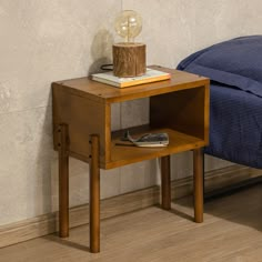 a small wooden table with a lamp on top of it next to a blue bed