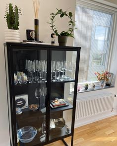 a display case with wine glasses and plates on it in front of a potted plant